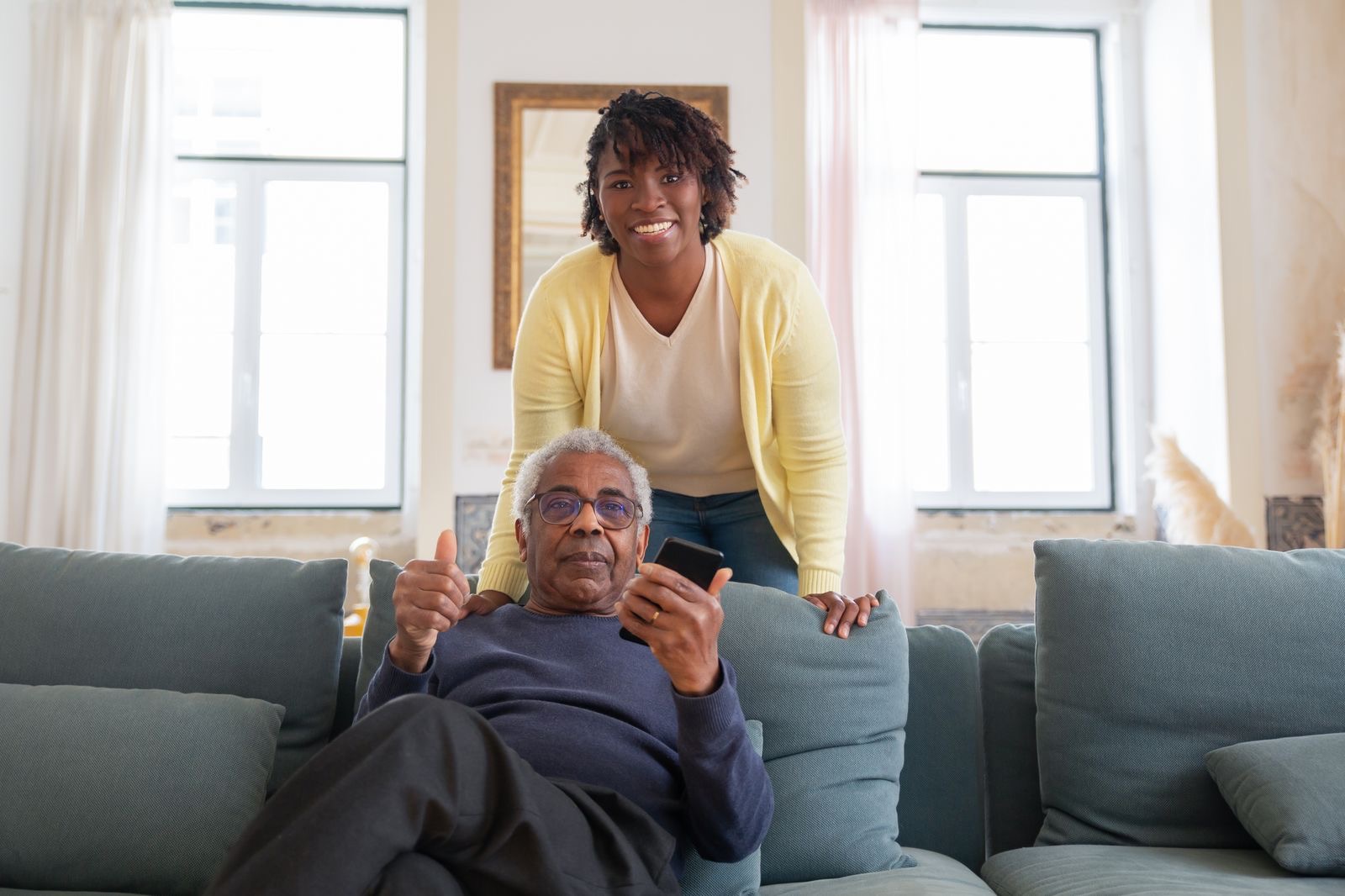 An older man smiling on his couch with his caregiver beside him