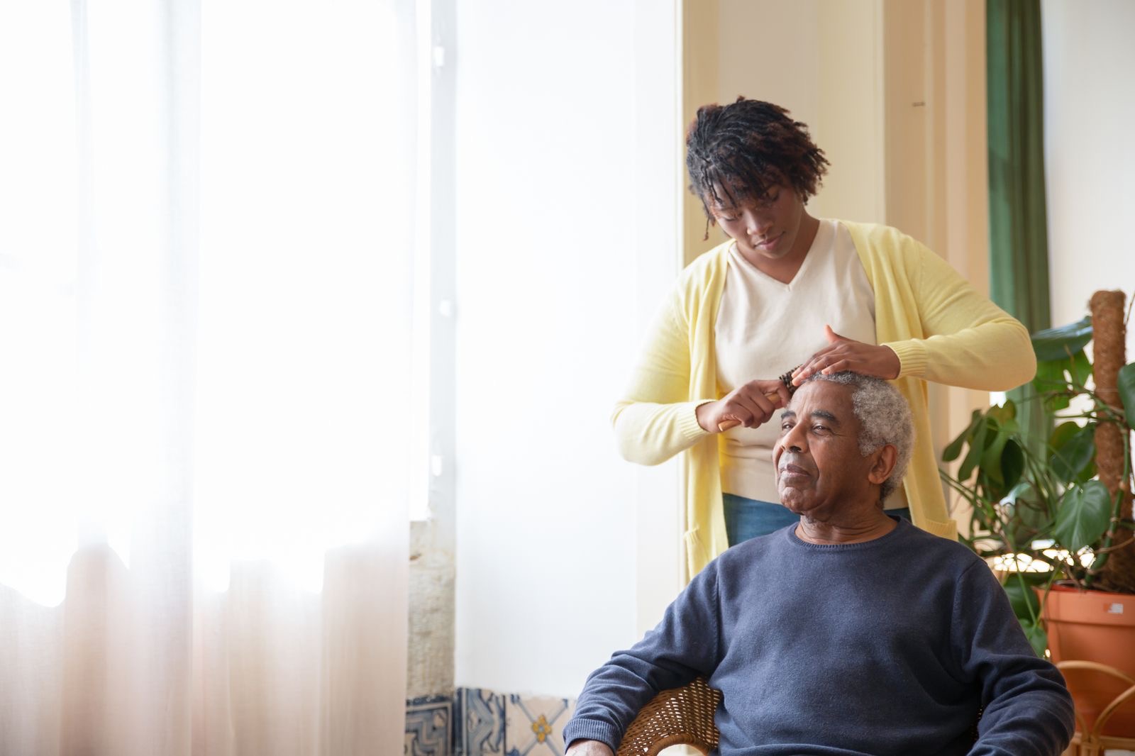 A caregiver combing an older man’s hair at home