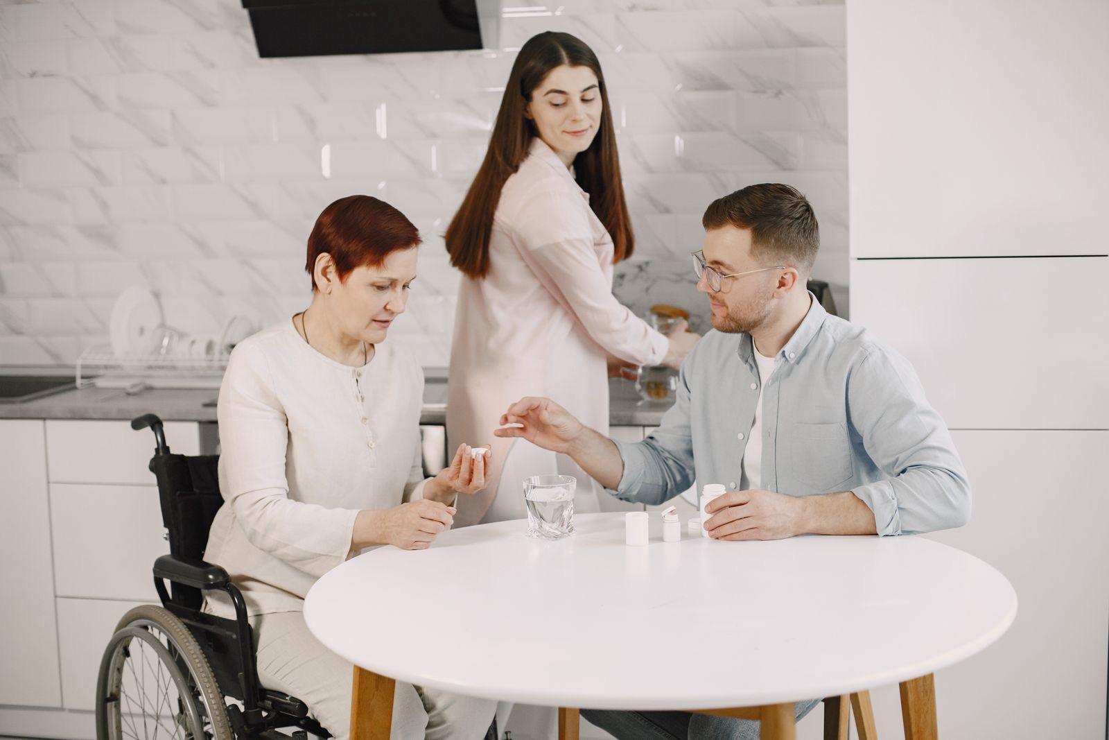 A caregiver helping an older woman with her medication at the kitchen table
