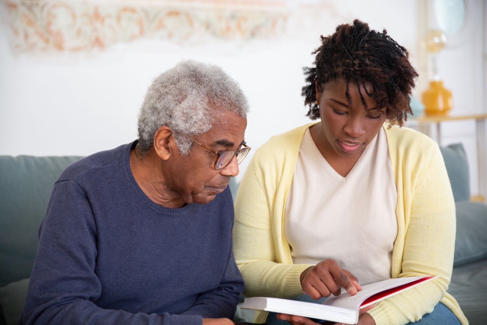 A caregiver reading with an older man on the couch
